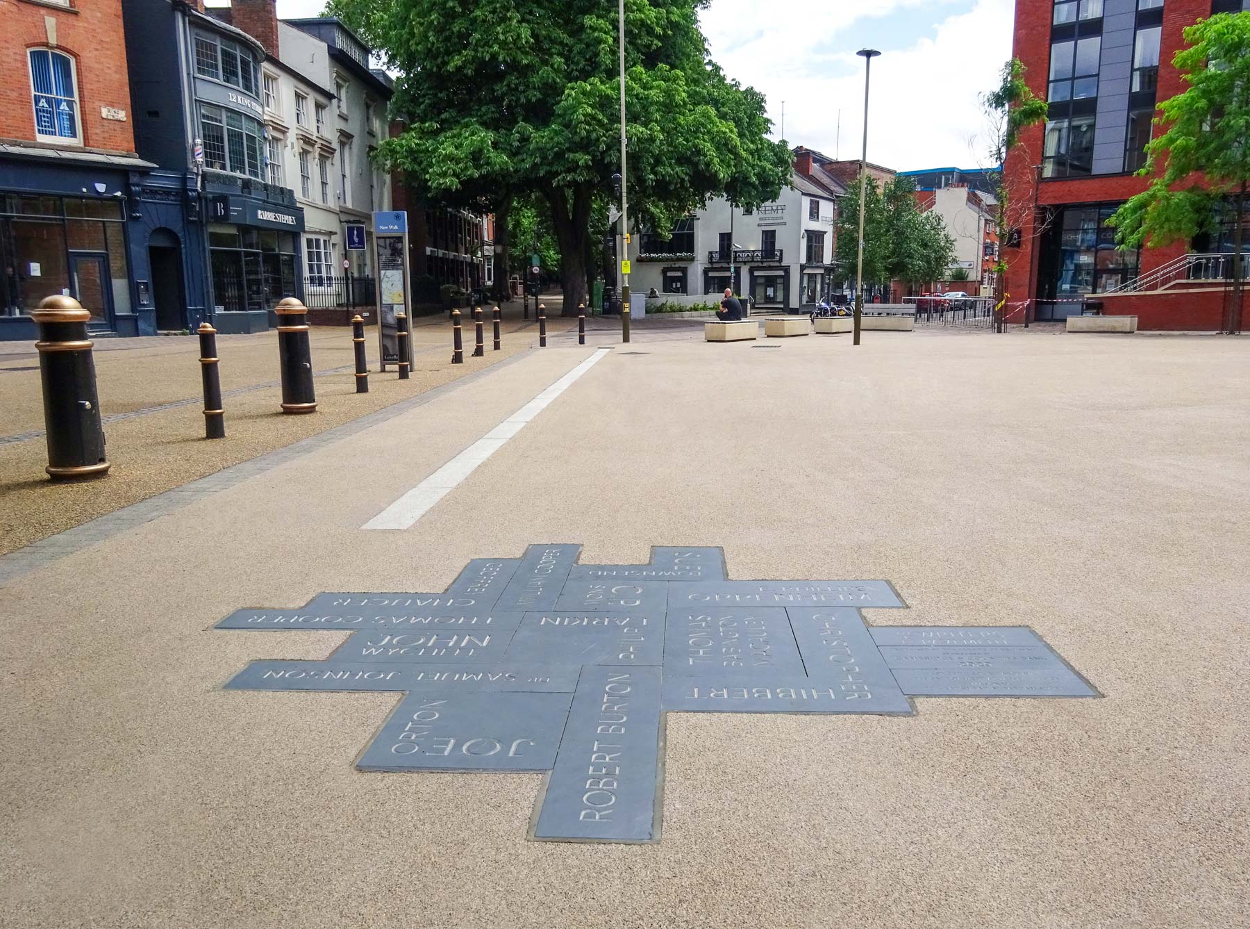 Photograph of The Writers' Pavement which is a stone carved typographic peice, embeded into the floor surfacing in the piaza, showing the bars on the left with the direction up New Walk to Upper New Walk in the distance